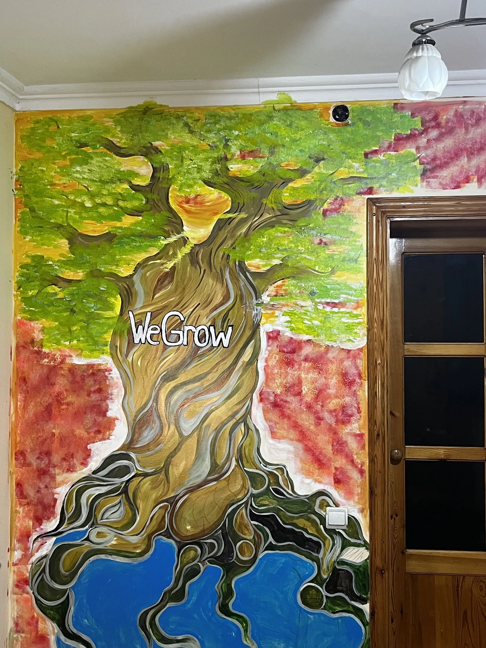 WeGrow tree mural painted on a wall at home โ a tree growing out of the earth with WeGrow written on the trunk